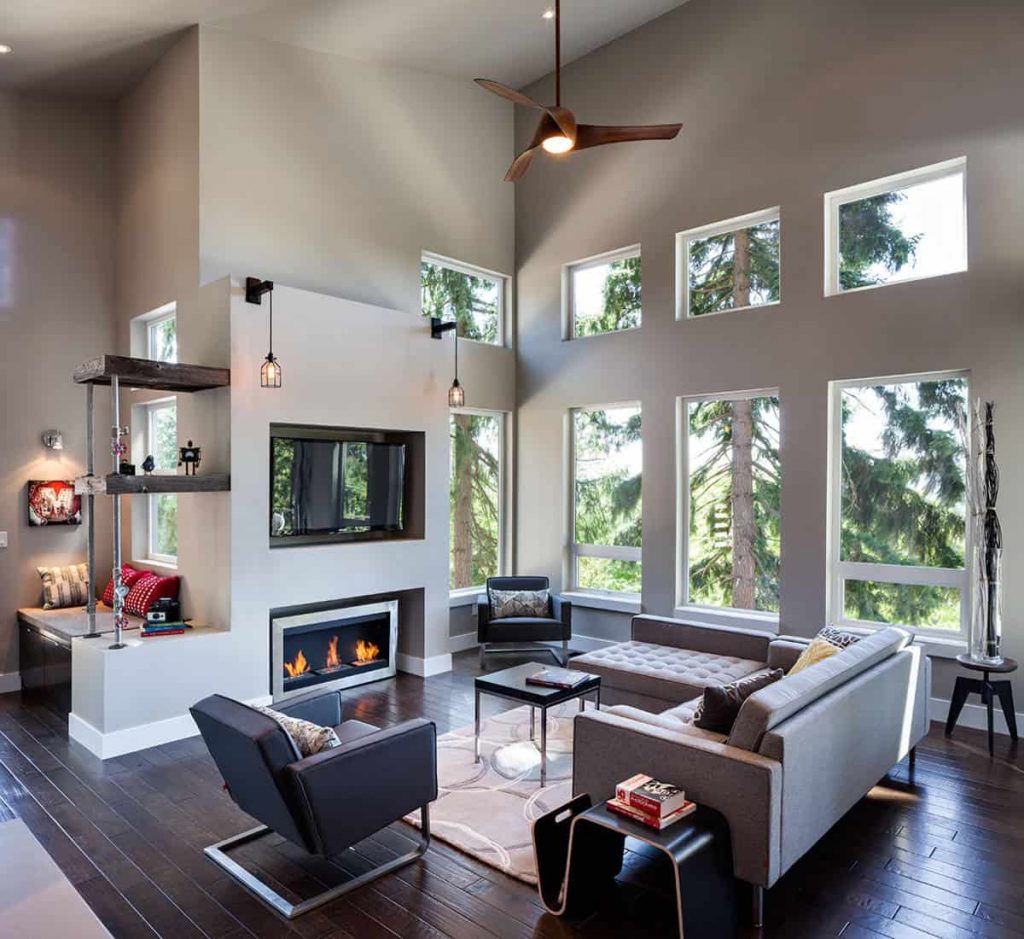 Medium-sized living room in a house with wooden floor, window wall, grey walls and sofas, black chairs, small fireplace in a niche and a TV above the fireplace