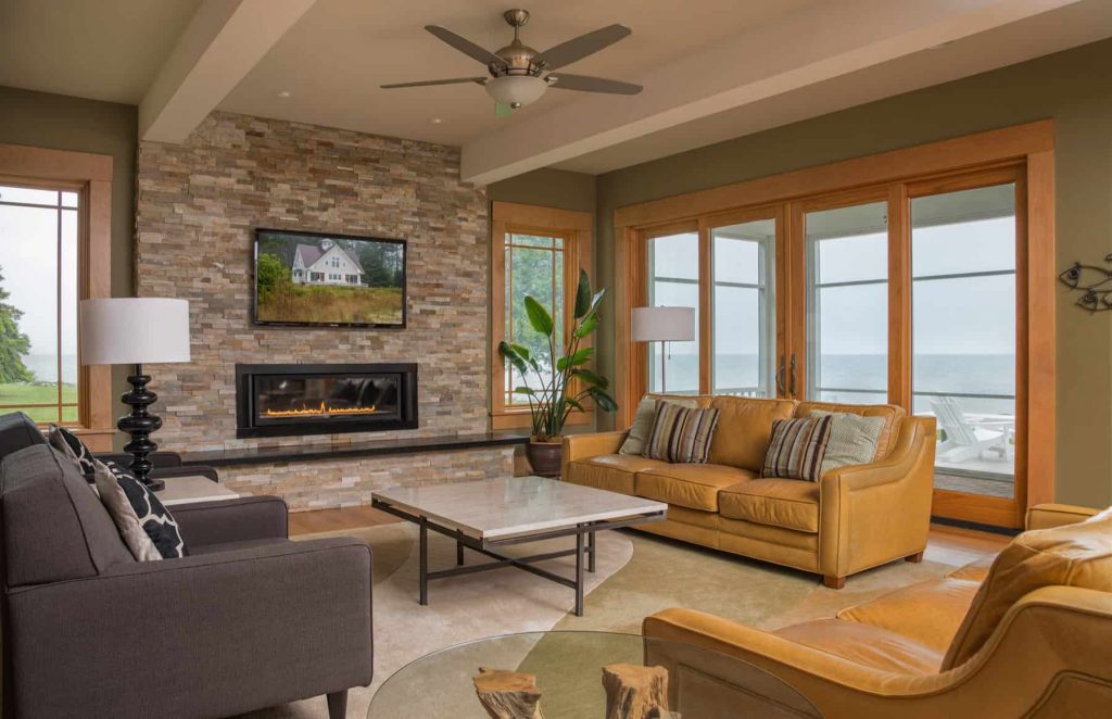 Medium-sized living room in a house with a view of the sea, green walls, brown and grey sofas, small fireplace in a stone tile wall and a TV above the fireplace