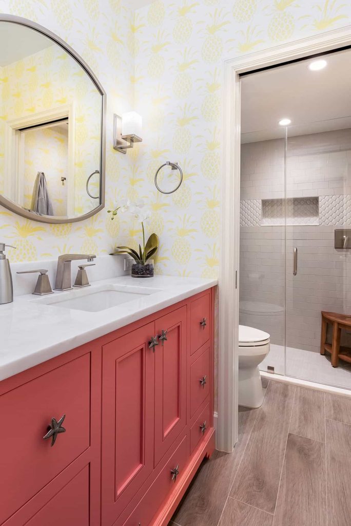 White tile shower, coral cabinets, yellow pineapple pattern wallpaper