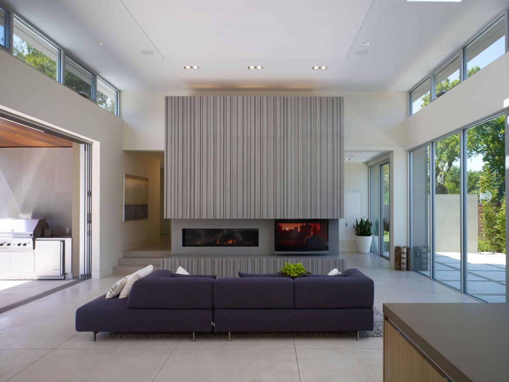 Spacious living room grey tile floor, window wall, purple sofa, grey textured wall with a wide fireplace and a TV next to the fireplace