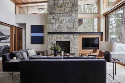 Spacious living room interior in a house with window wall, sofa, chairs, white walls and a stone fireplace