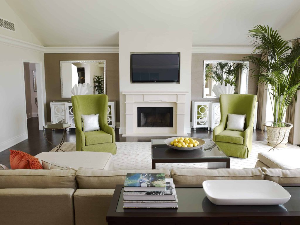 Medium living room in a house with wooden floor, beige sofa and green chairs, small fireplace and a TV above the fireplace