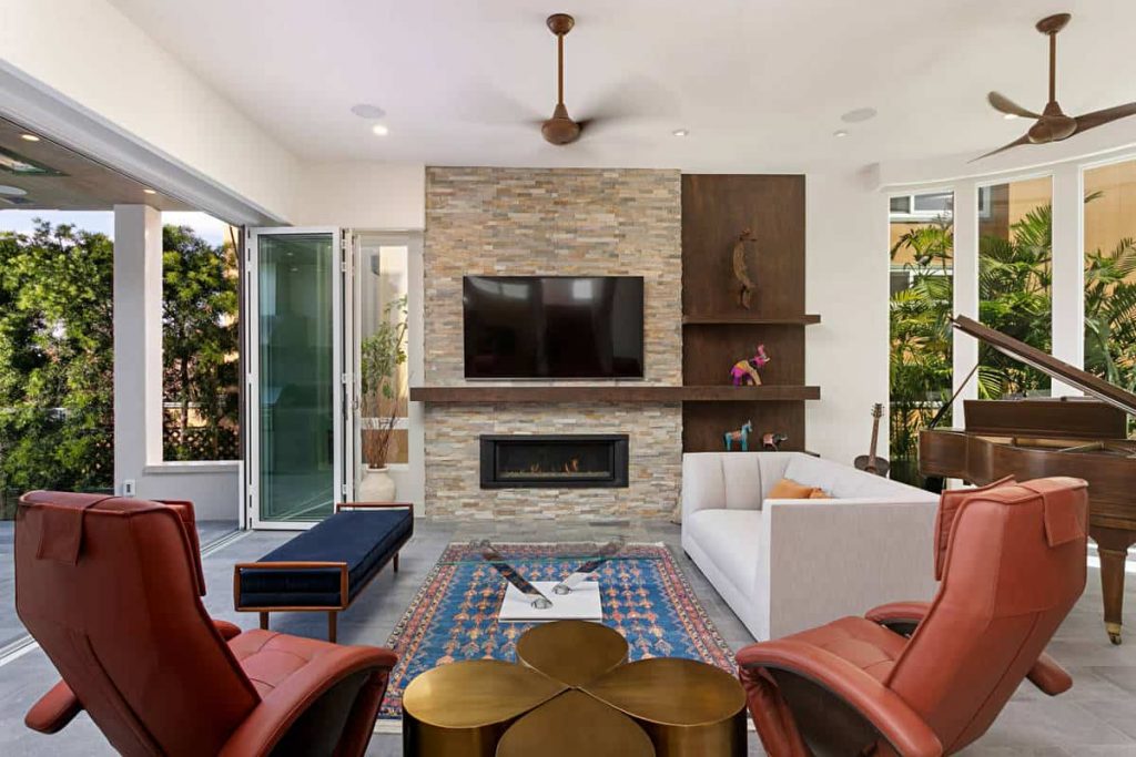 Medium-sized living room with a balcony in an appartment with grey tile floor, white sofa and red-brown chairs, piano, small brick fireplace and a TV above the fireplace