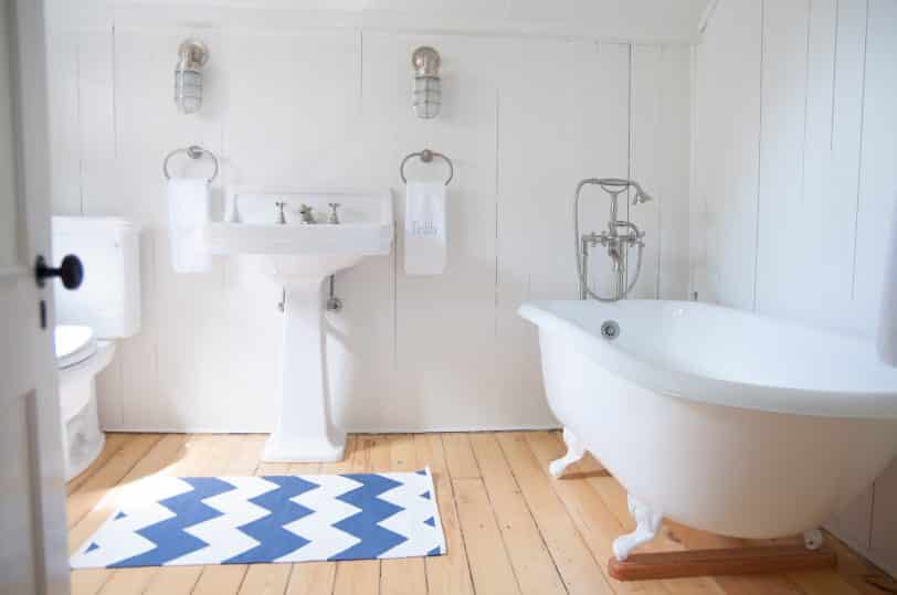 Inspiration for a mid-sized coastal master light wood floor claw-foot bathtub remodel in Other with a two-piece toilet, white walls and a pedestal sink