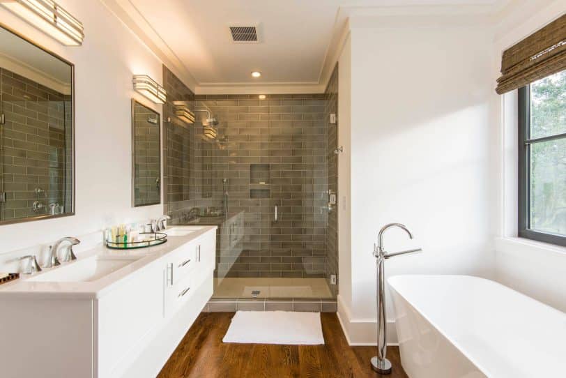 Inspiration for a mid-sized transitional master gray tile and porcelain tile medium tone wood floor bathroom remodel in Charleston with shaker cabinets, white cabinets, white walls, an undermount sink, quartz countertops, a hinged shower door and white countertops
