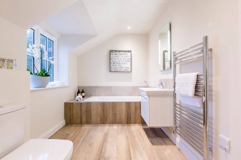 Example of a trendy brown tile alcove bathtub design in London with flat-panel cabinets, white cabinets, white walls, a console sink and a two-piece toilet