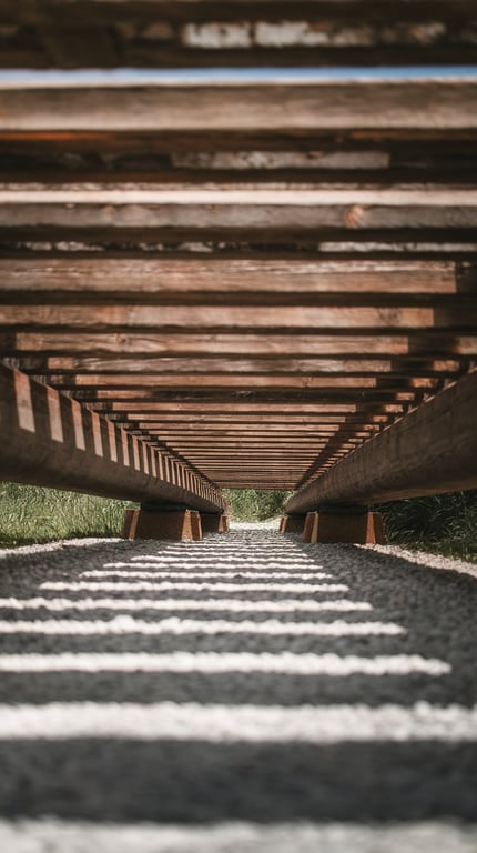 View under a wooden footbridge showing a gravel creek bed.