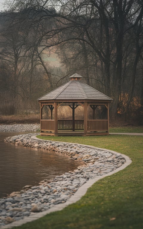 A wooden gazebo surrounded by a river rock base along a water body.
